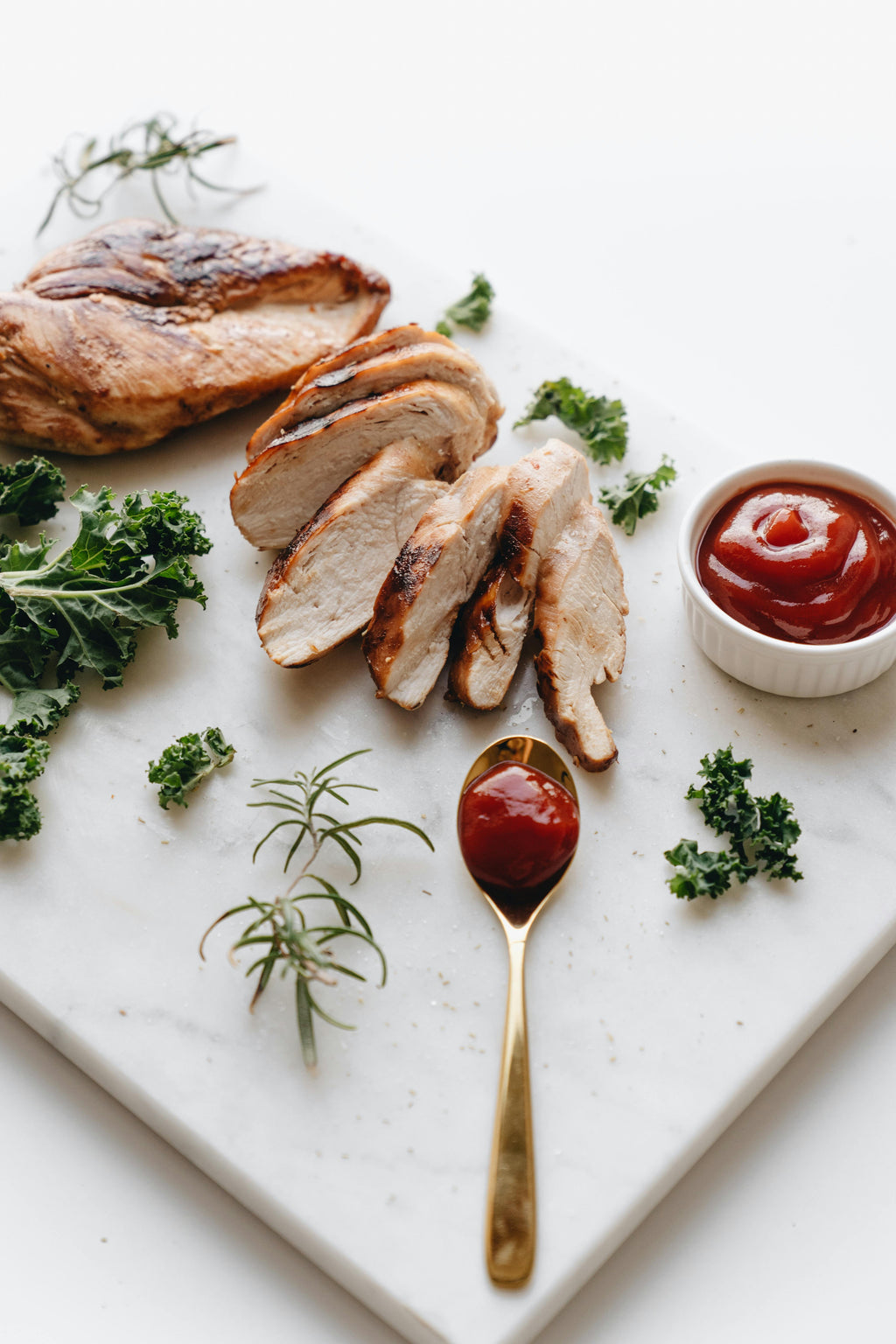 Sliced chicken breast on a marble board with herbs and ketchup.