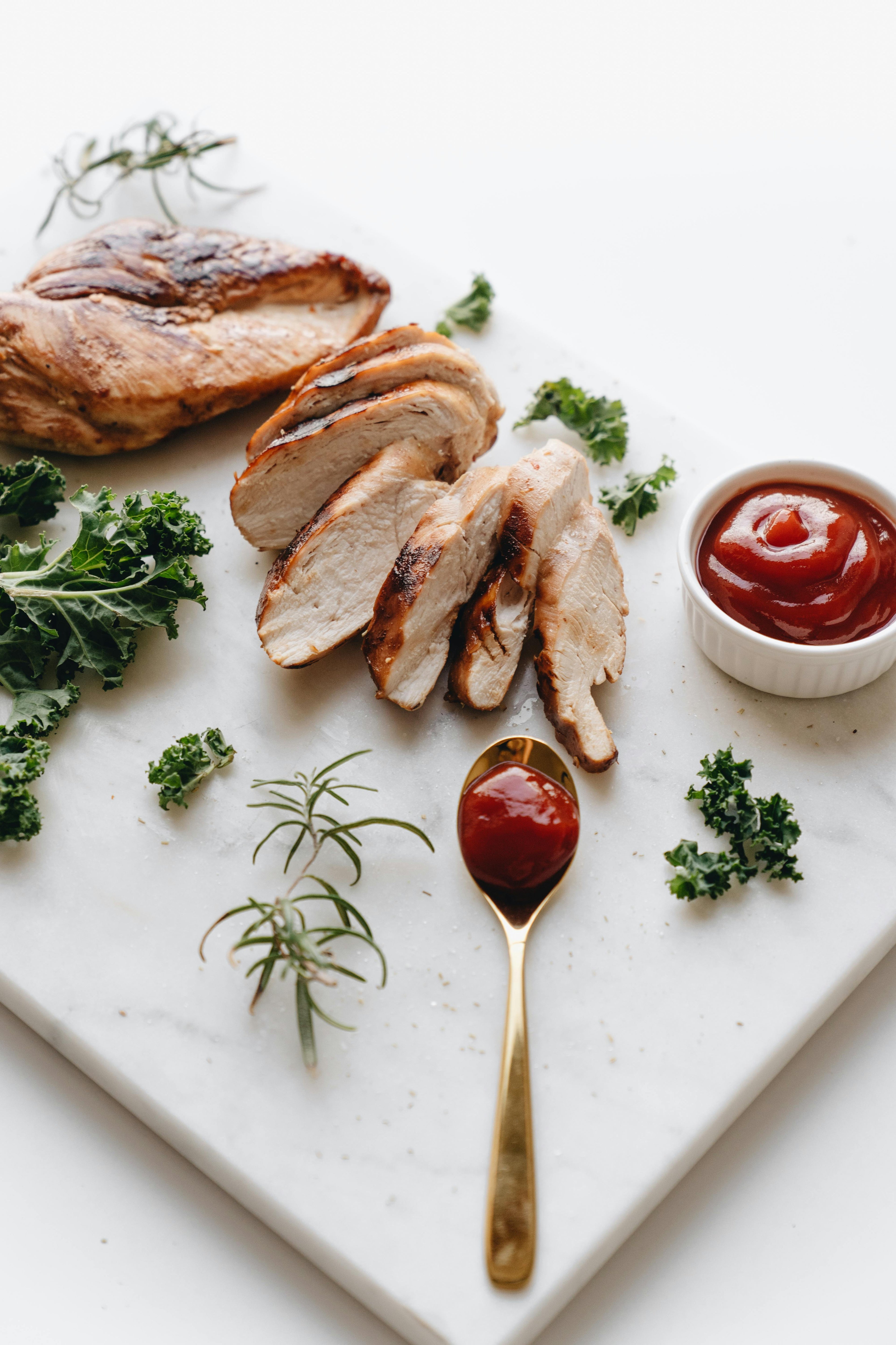 Sliced chicken breast on a marble board with herbs and ketchup.