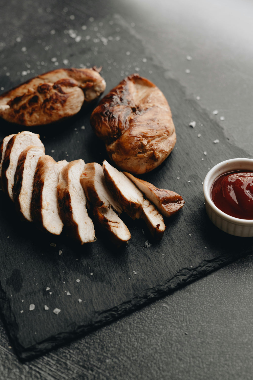 Sliced chicken breast on a dark slate board with a side of ketchup.
