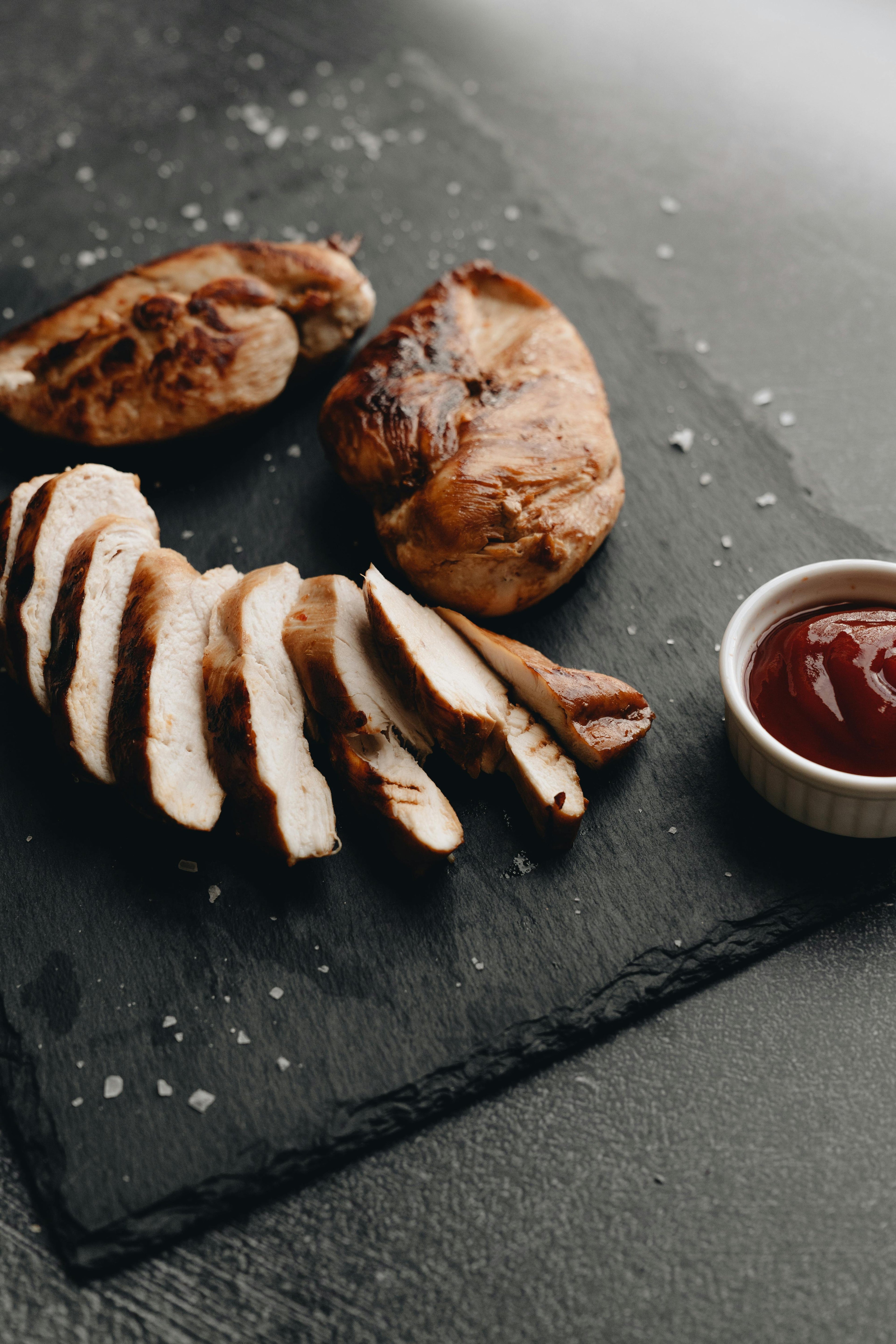 Sliced chicken breast on a dark slate board with a side of ketchup.