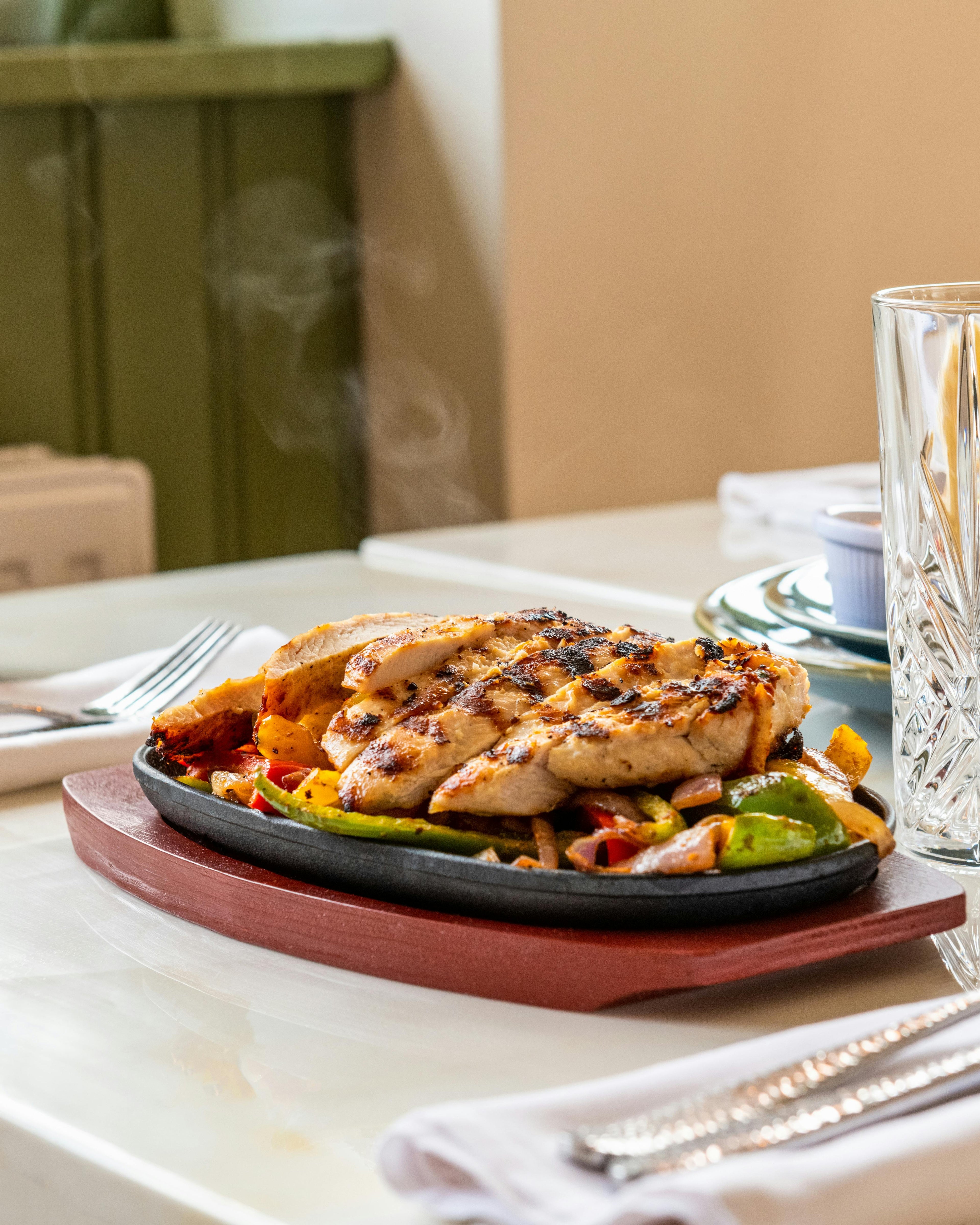 Plated dish of grilled chicken with vegetables on a wooden tray, set on a table.